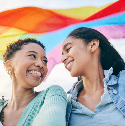 Two smiling women under a rainbow banner