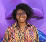 Woman smiles at camera, wearing a colorful blouse, against a purple background.