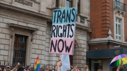 a person holding a "trans rights now" sign during an LGBTQ+ rights protest.